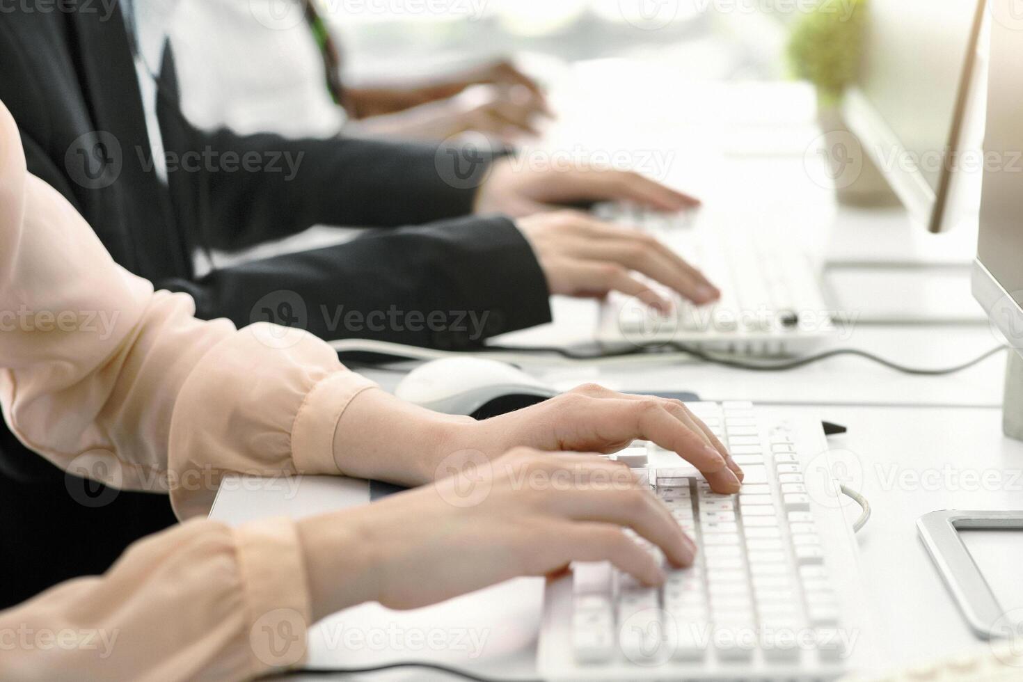 Cropped view of customer support operators at work in modern call centre, copy space. Team of young hotline consultants using computers at open space office, closeup of hands photo
