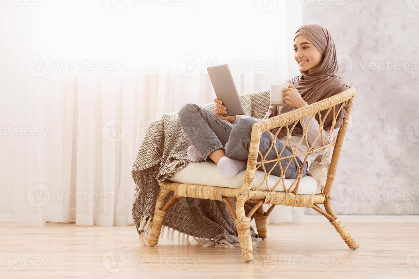 Young Arabic Girl In Hijab Relaxing In Modern Chair With Coffee And Digital Tablet, Enjoying Time At Home, Copy Space photo