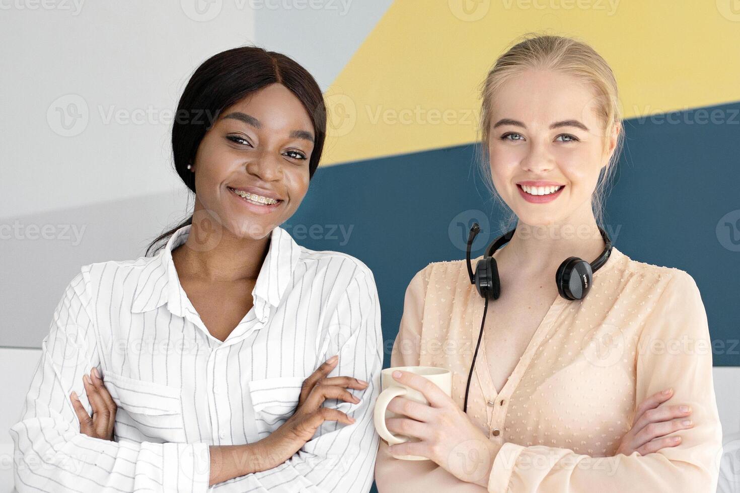 Portrait of female call centre operators smiling and looking at camera during their coffee break at modern office, free space. Positive customer support agents posing at workplace photo