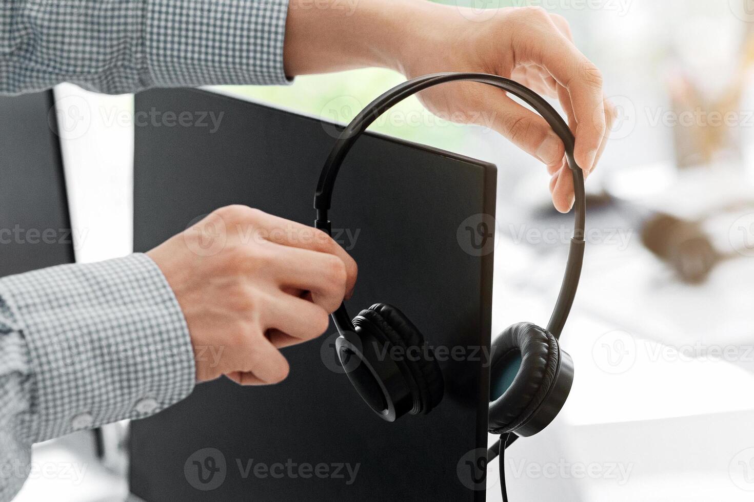 Contact center worker placing his headset on computer monitor at office, close up of hands. Copy space photo