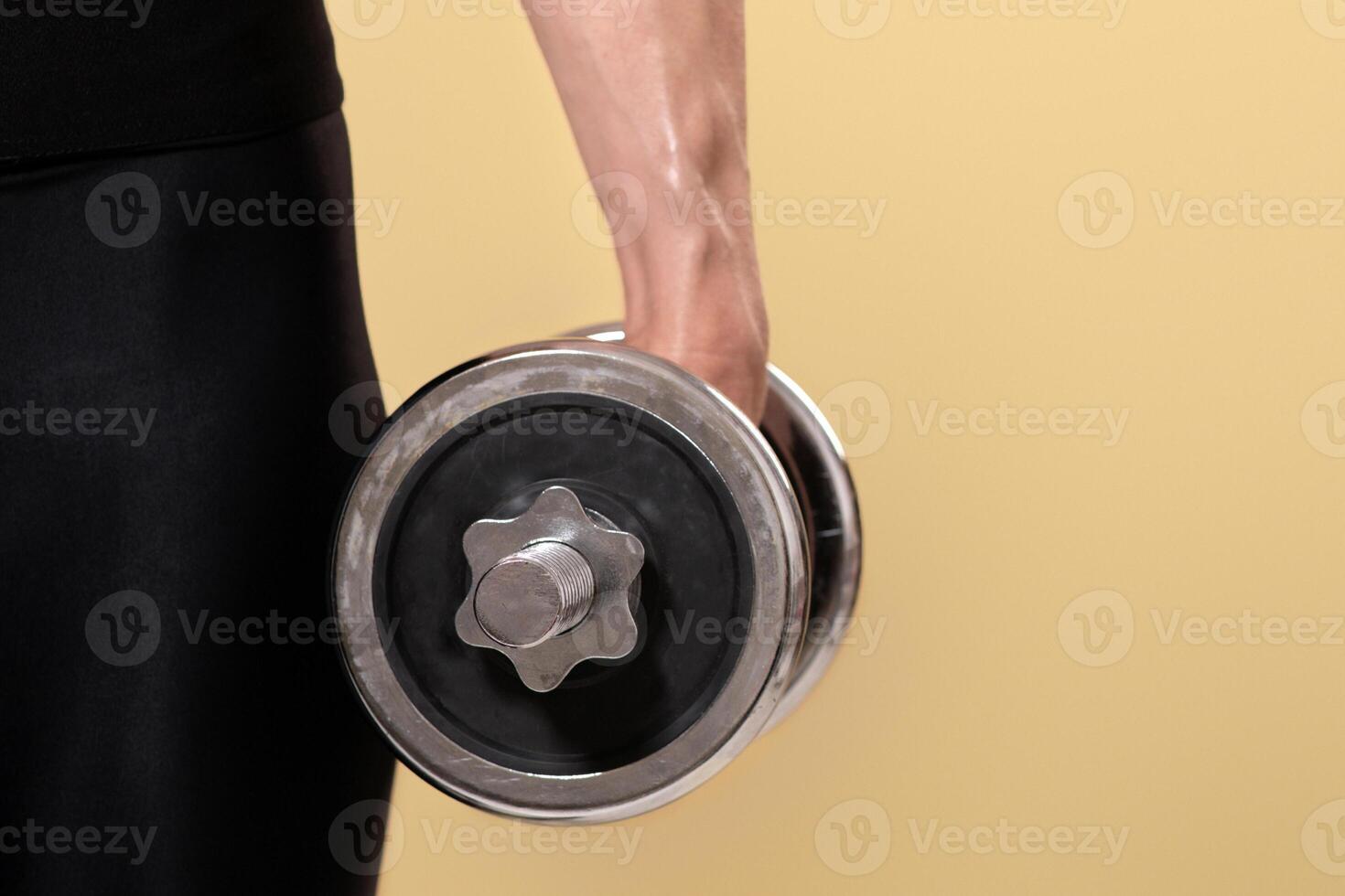 Middle aged fitness blogger and popular trainer and ad space. Hand of muscular adult female doing dumbbell exercise, isolated on beige background, empty space, close up, cropped, studio shot photo
