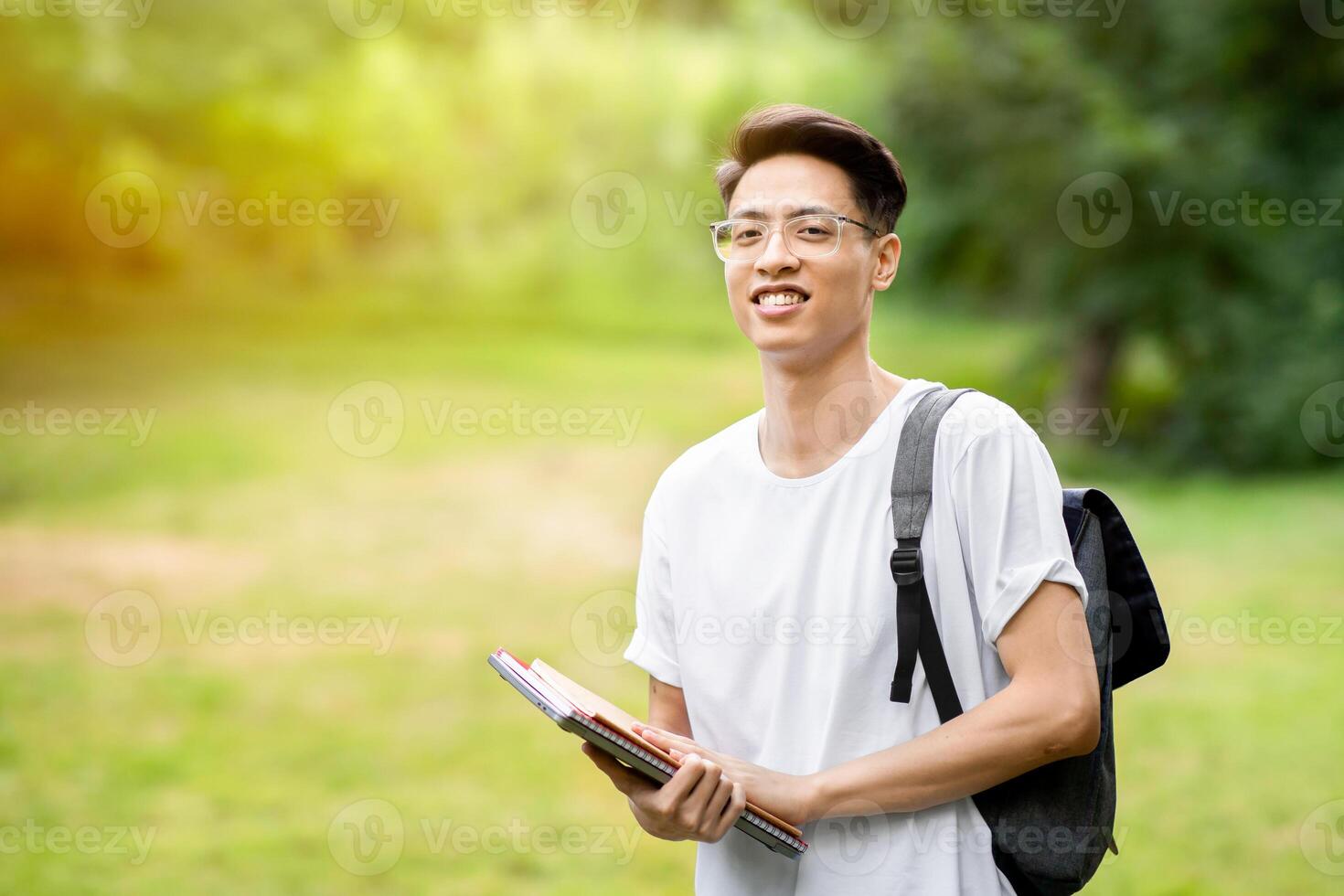Portrait of smiling asian student guy with backpack and workbooks posing outdoor in college courtyard, looking at camera, copy space photo