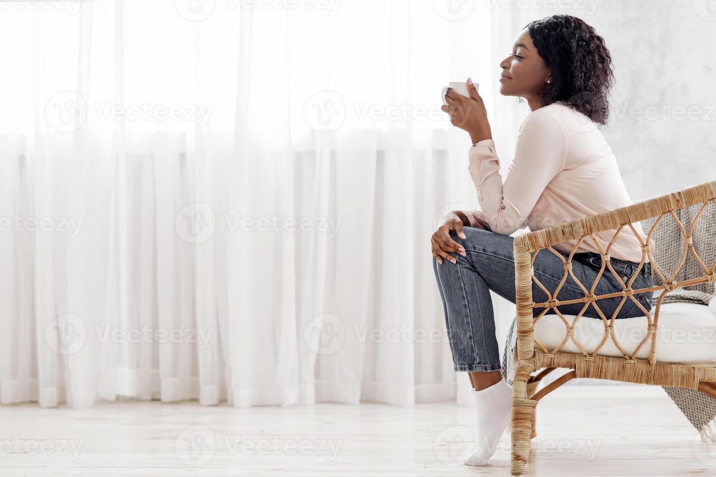 Relaxing Morning. Side View Portrait Of Calm Black Female Sitting In Wicker Chair Enjoying Coffee, Resting At Home In Living Room, Drinking Hot Tea, Holding White Mug, Side View With Copy Space photo