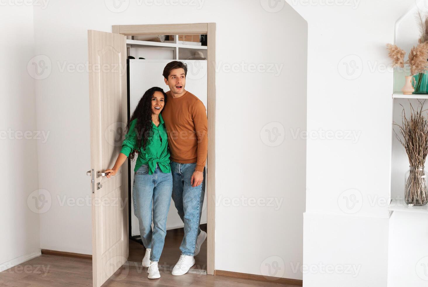 Wow. Portrait of excited emotional couple walking in their apartment, entering new home, happy young guy and lady standing in doorway of modern flat, looking at design interior together, coming inside photo