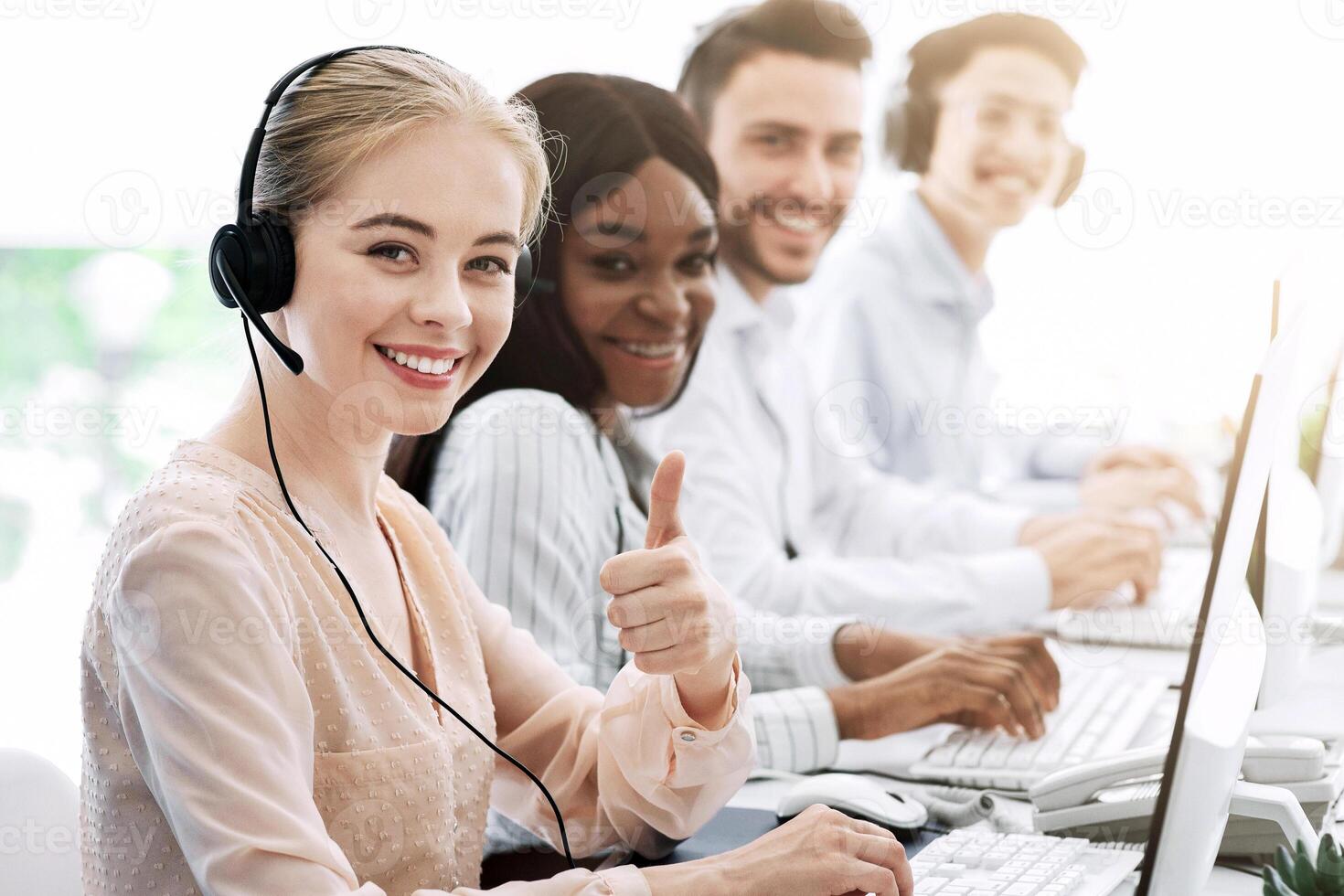 Multiethnic call centre consultants with headsets smiling at camera in modern office photo