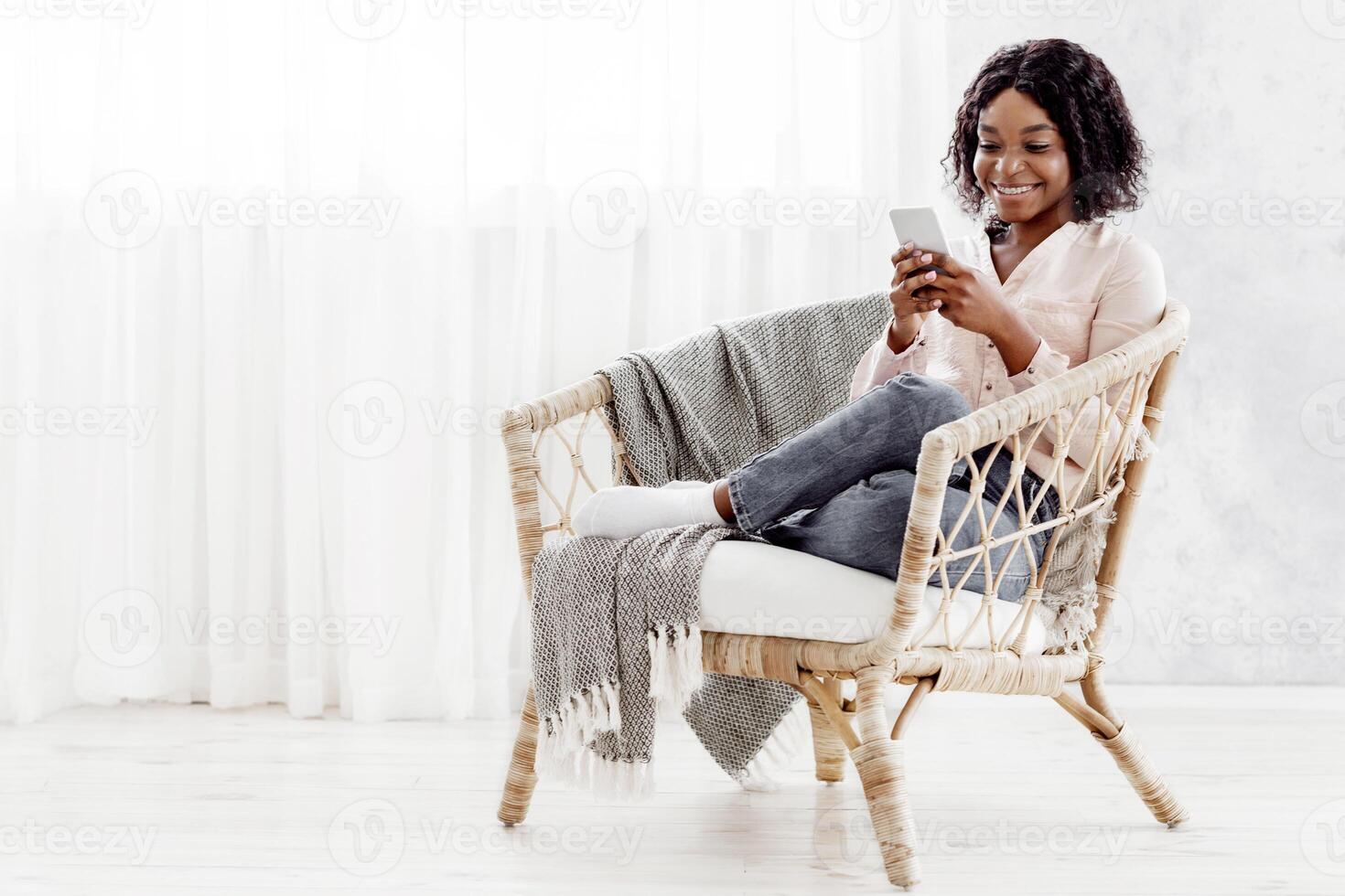 Relaxed Black Girl Sitting In Wicker Chair And Messaging On Smartphone At Home, Panorama With Copy Space photo