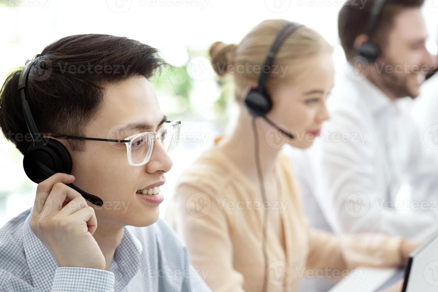 Asian hotline operator and his colleagues working at modern call centre office, copy space. Customer support agents in headsets providing services to clients, selling goods online photo