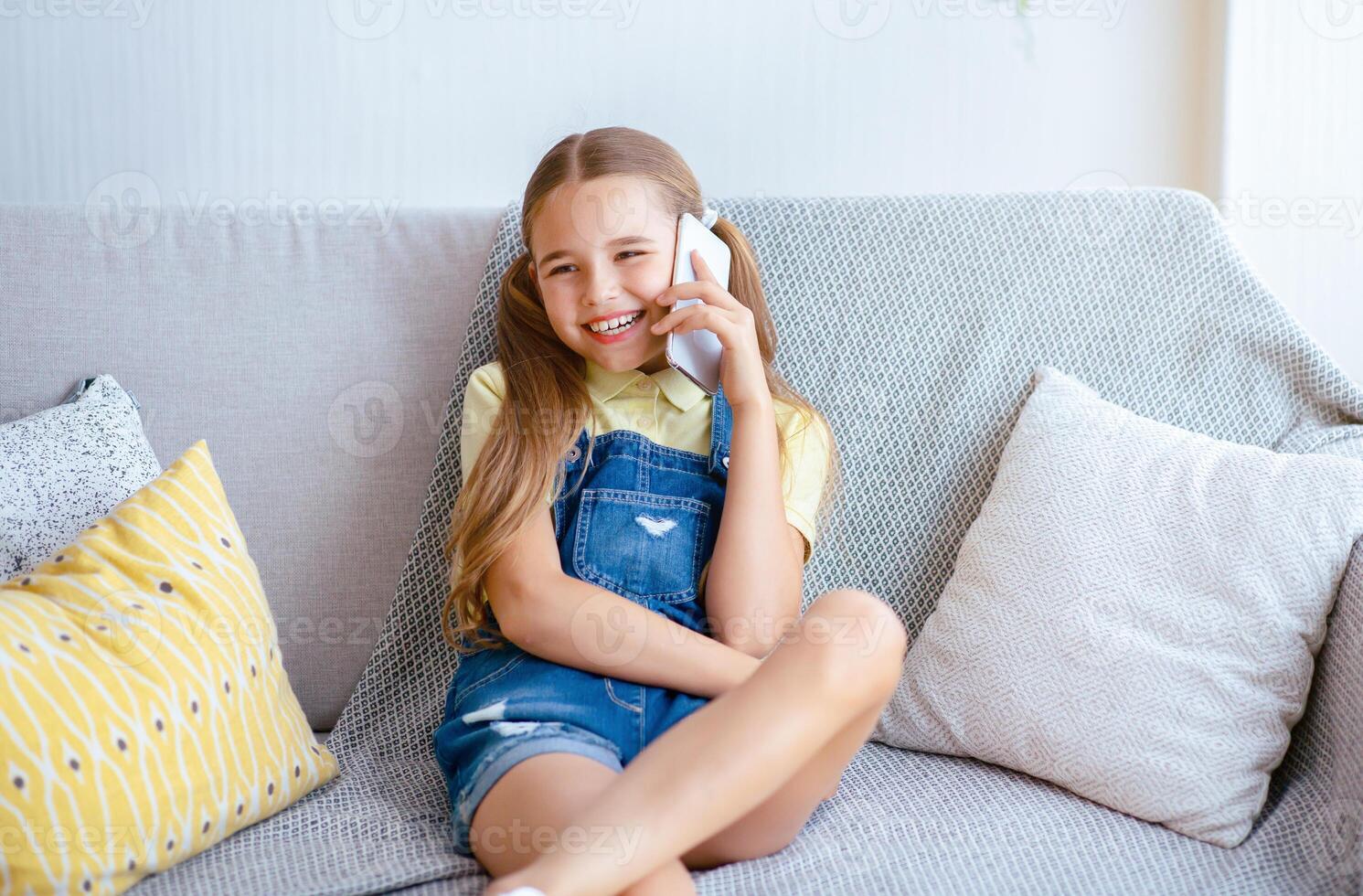 Pleasant Talk With Friend. Portrait of happy girl talking on smart phone sitting on the beige sofa with pillows photo