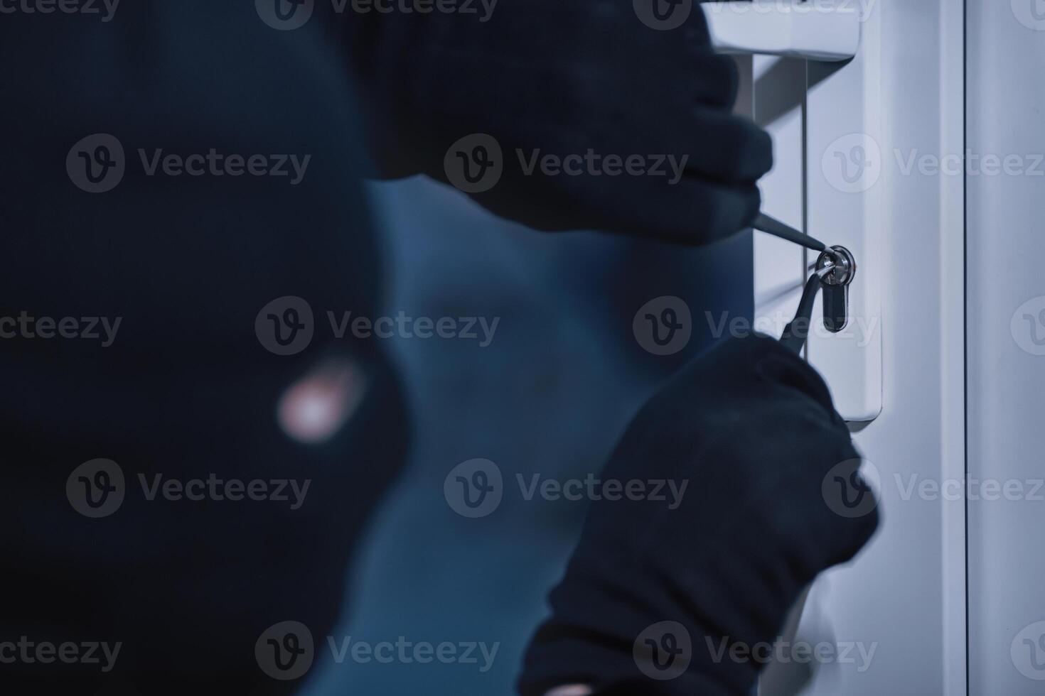 Closeup of robber in black mask cracking door lock with metal picklock tool during house breaking photo