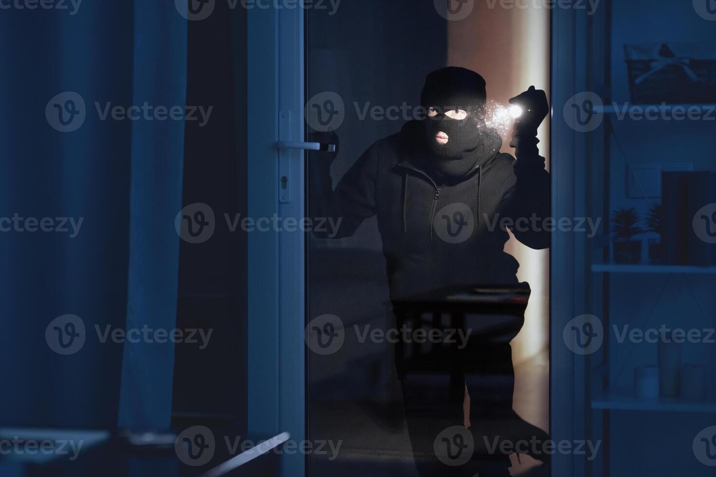 Vandalism Concept. Disguised villain with torch watching enclosed property through balcony glass door photo