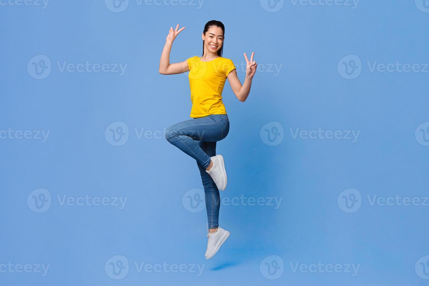 Carefree Mood. Cheerful Asian Girl Jumping In The Air And Showing Peace Gesture Over Purple Background, Full Length Shot With Free Space photo