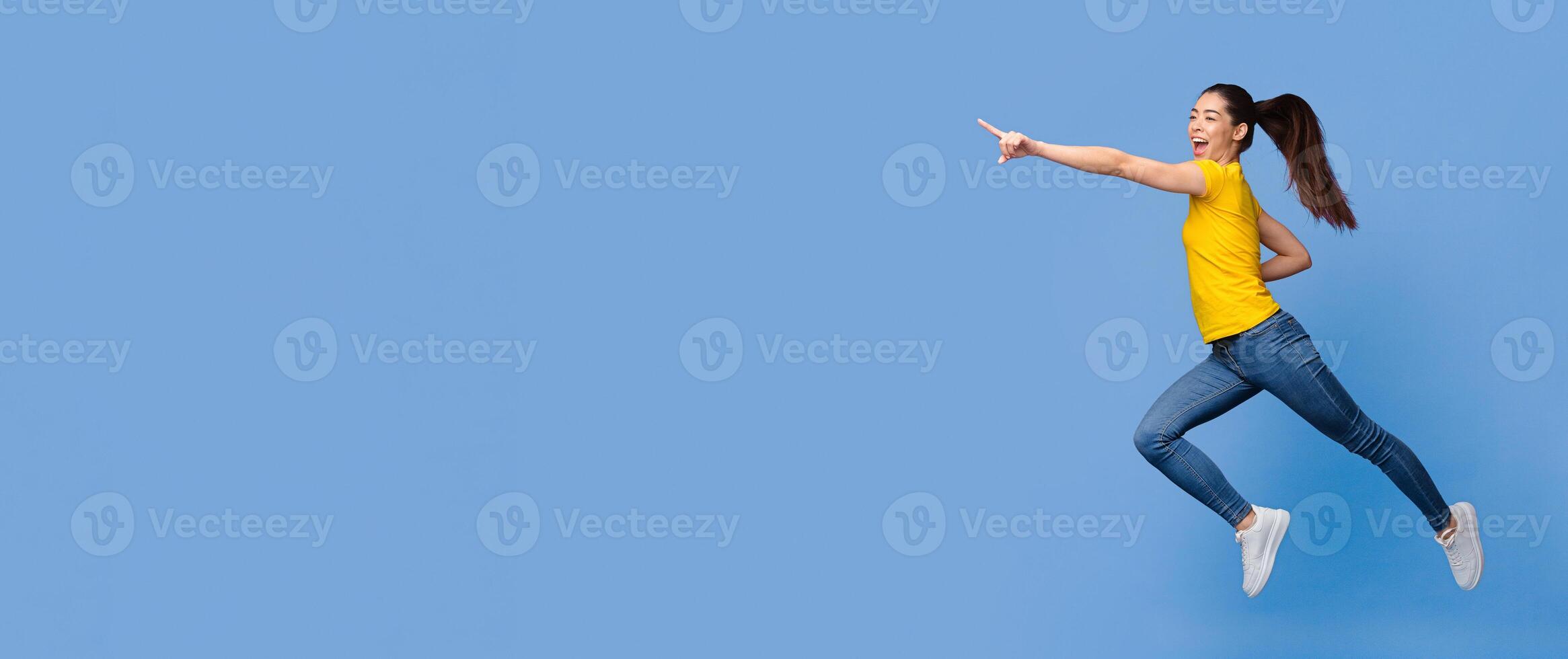Look there. Excited Asian Girl Jumping And Pointing Aside At Copy Space On Purple Background, Full-Lenght Shot, Panorama photo