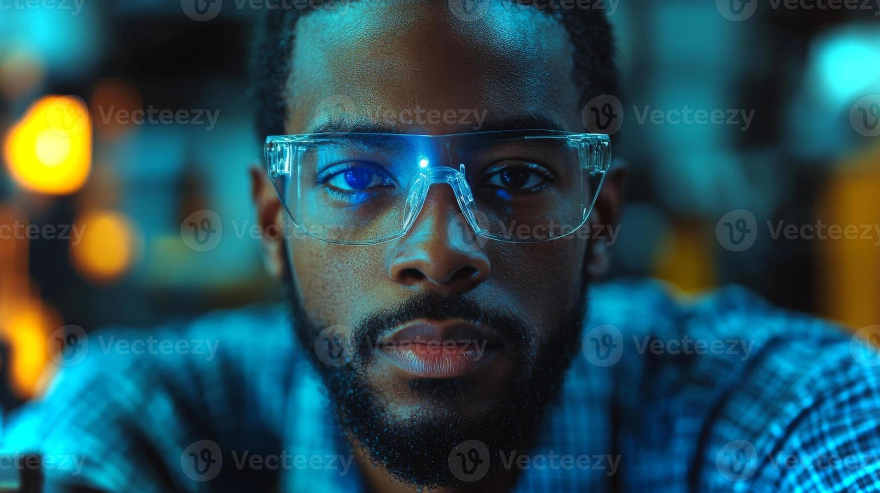 A dedicated engineer wearing safety glasses intensely focuses on machinery within a bustling manufacturing environment. The bright lights highlight his concentration on the assembly process. photo