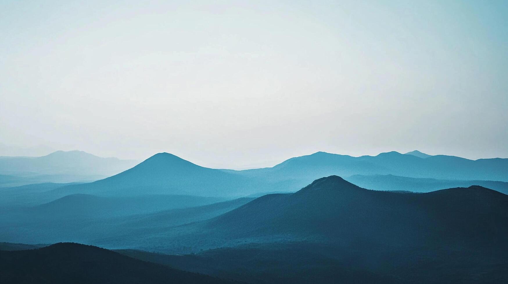 A serene view of layered blue mountains in soft morning light, creating a peaceful and tranquil atmosphere ideal for outdoor enthusiasts and nature lovers. photo