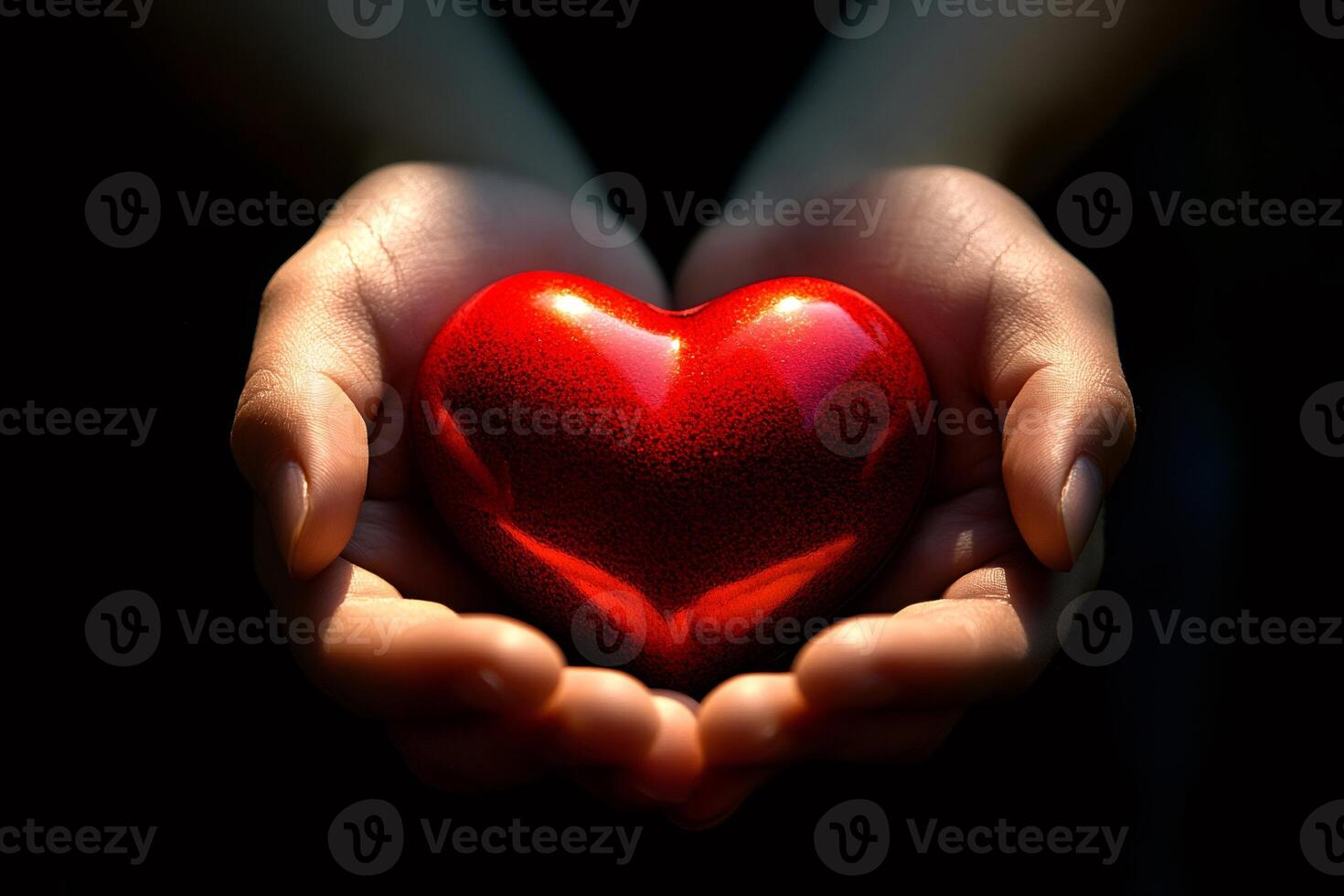 Two hands holding a shiny red heart against black background photo