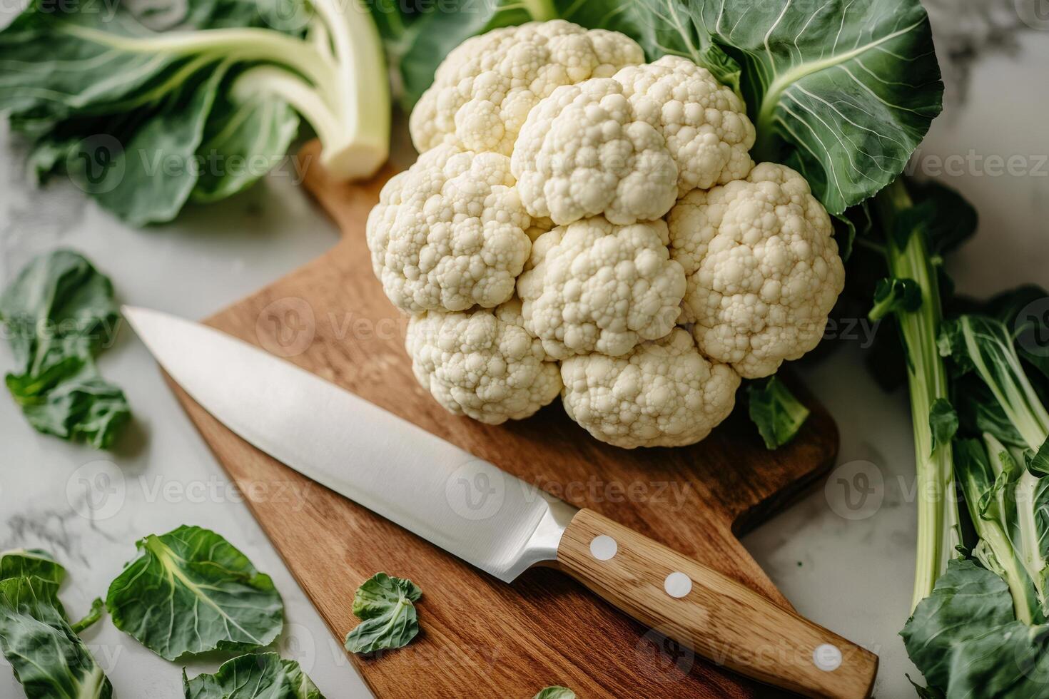 Chef preparing fresh cauliflower on wooden cutting board with sharp knife photo