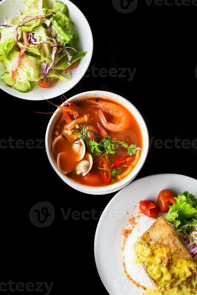 Lunch set made of tom yum soup, salad, grilled basa fish, rice, on black background photo