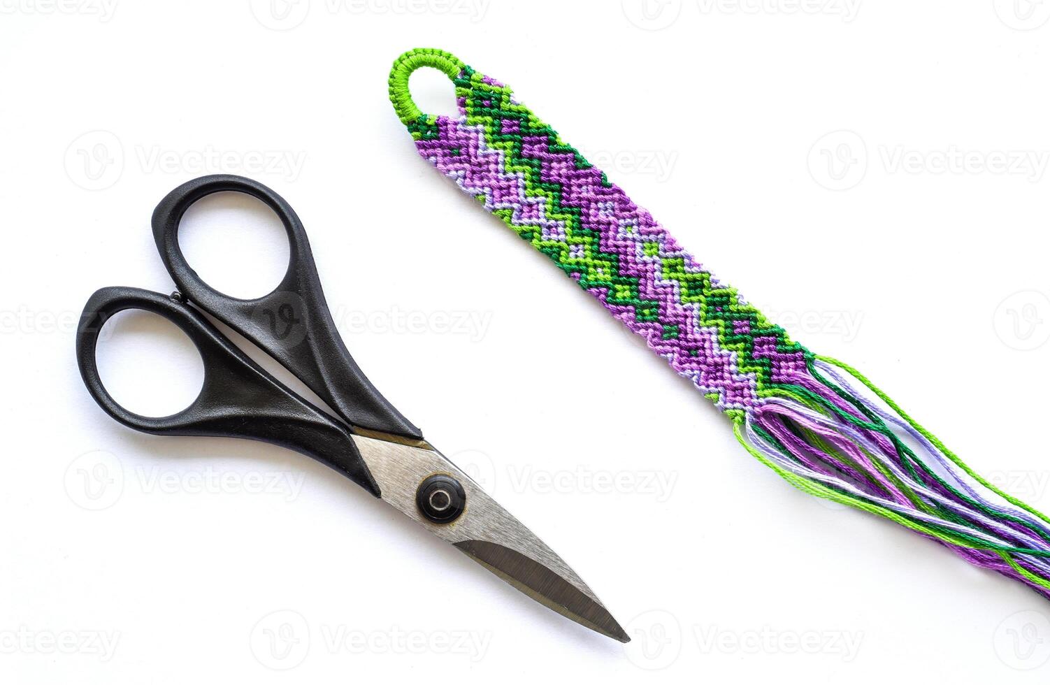 Unfinished woven DIY friendship bracelet with geyser pattern next to scissors on white background. Pastel colors photo