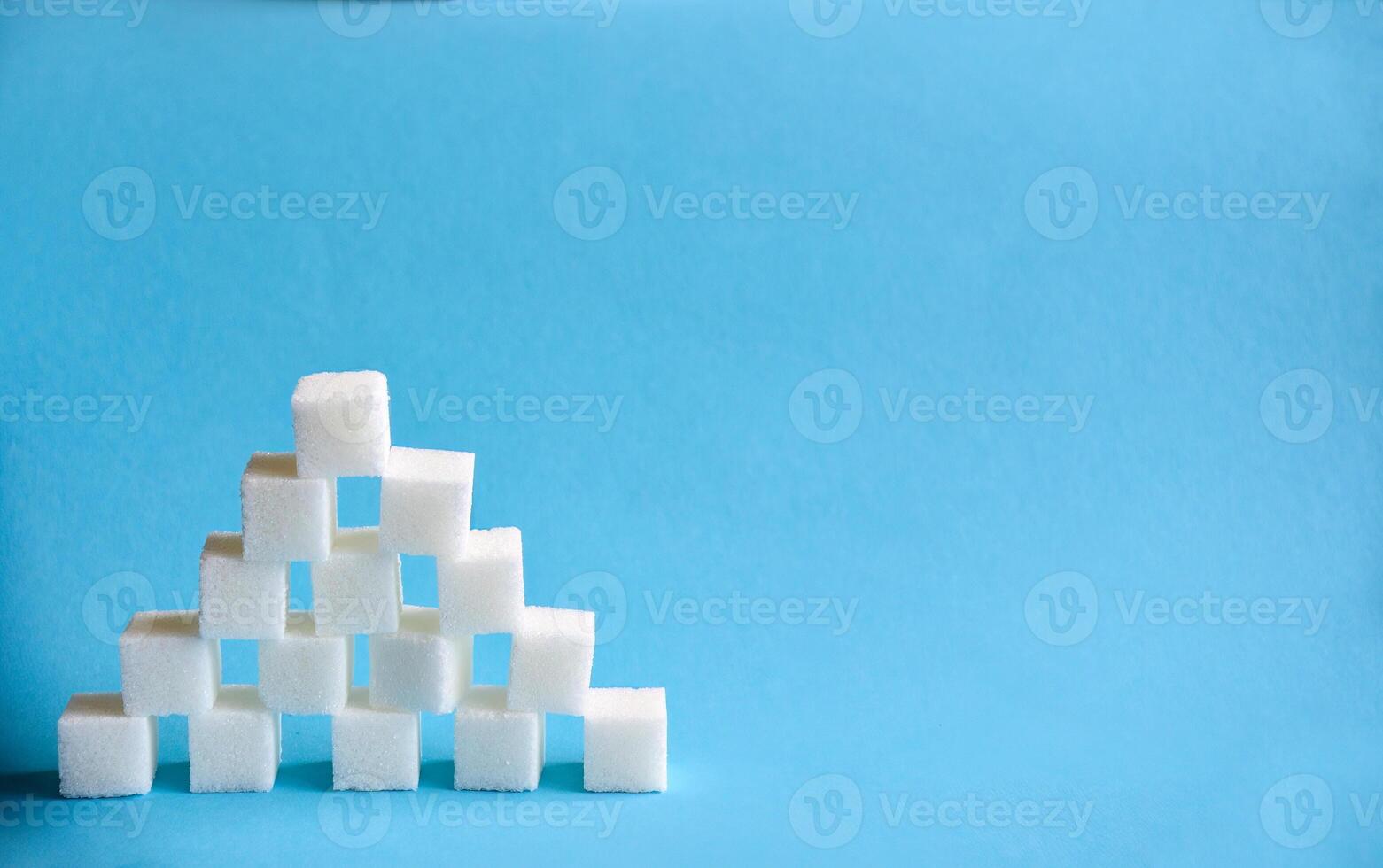 Pyramid made from cubes of refined white sugar on blue background. Copy space photo