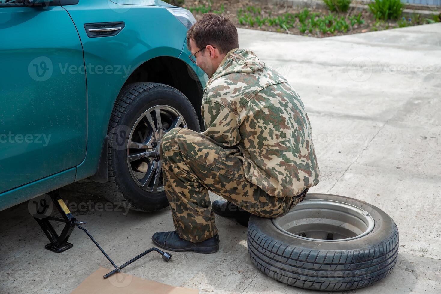 young man changing car tire for winter tires photo