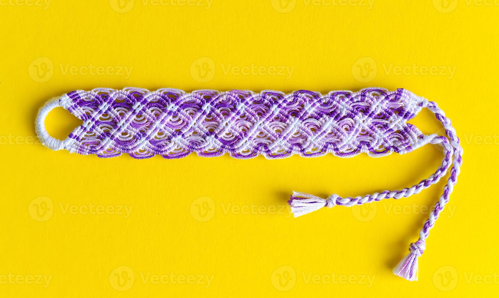 Lilac DIY friendship bracelet with unusual braiding on yellow background photo