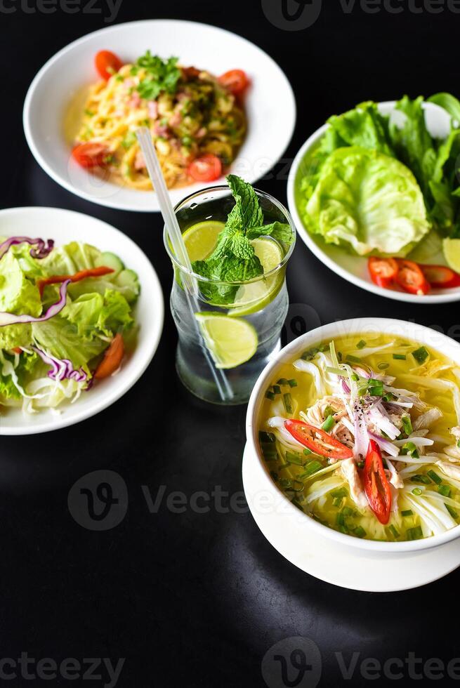 Lunch set made of chicken soup, salad banh mi,pasta carbonara, lemonade on black background photo