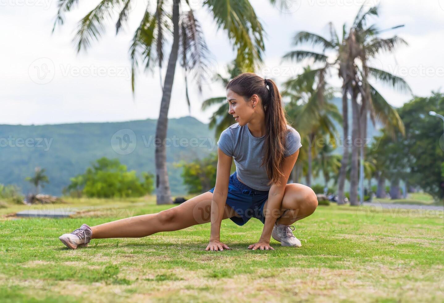 Young slim woman squatting and doing sport exercises against sunset and beach with palms photo