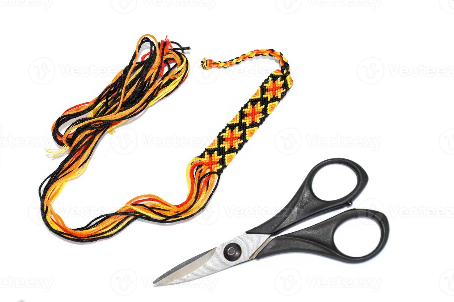 Unfinished woven DIY friendship bracelet with boho pattern next to scissors on a white background photo