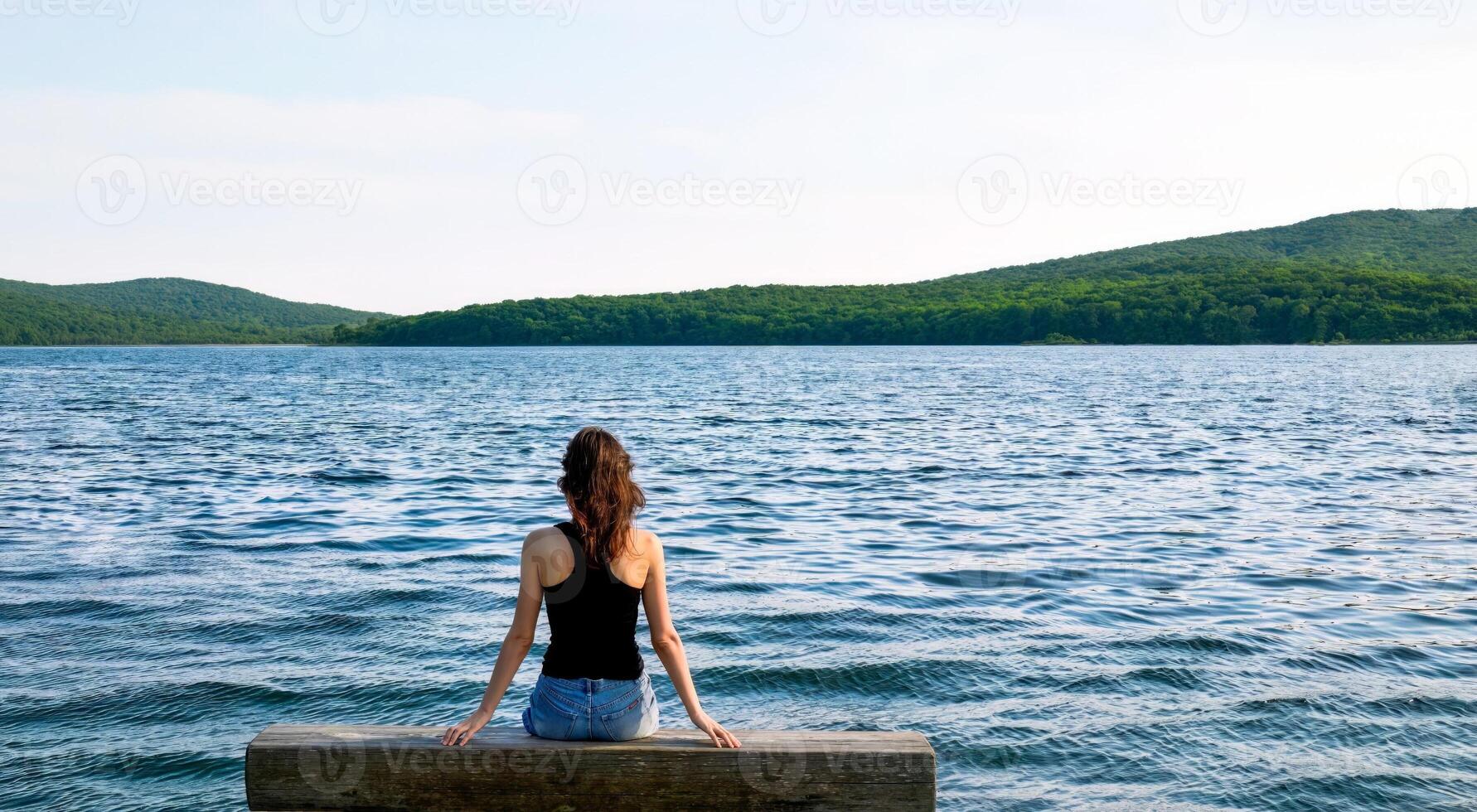 Brunette woman sitting on wooden bench on the pier on a dark evening against the background of the sea and forest. Copy space on top and side photo