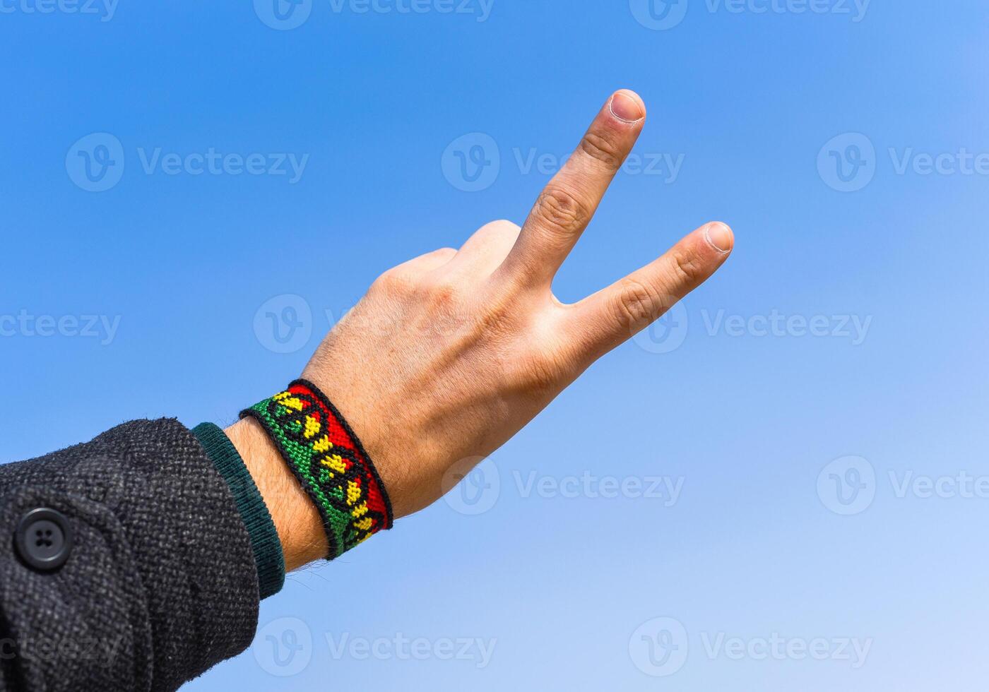 Handmade DIY friendship bracelet with Rasta flag pattern with a peace symbol on male wrist on sky background. photo