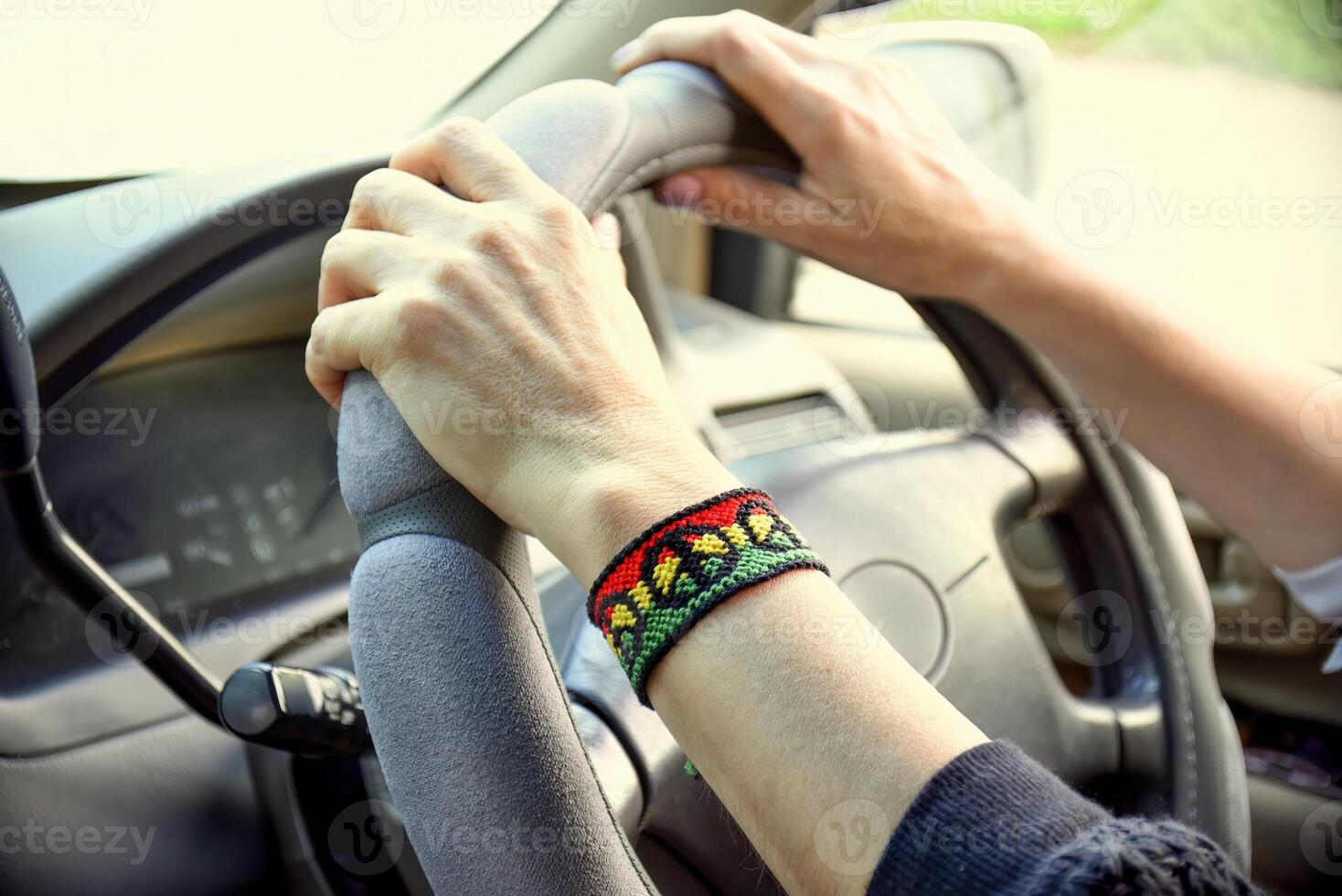 Handmade DIY friendship bracelet with Rasta flag pattern with a peace symbol on womens wrist. Hands holding steering wheel in the car. photo