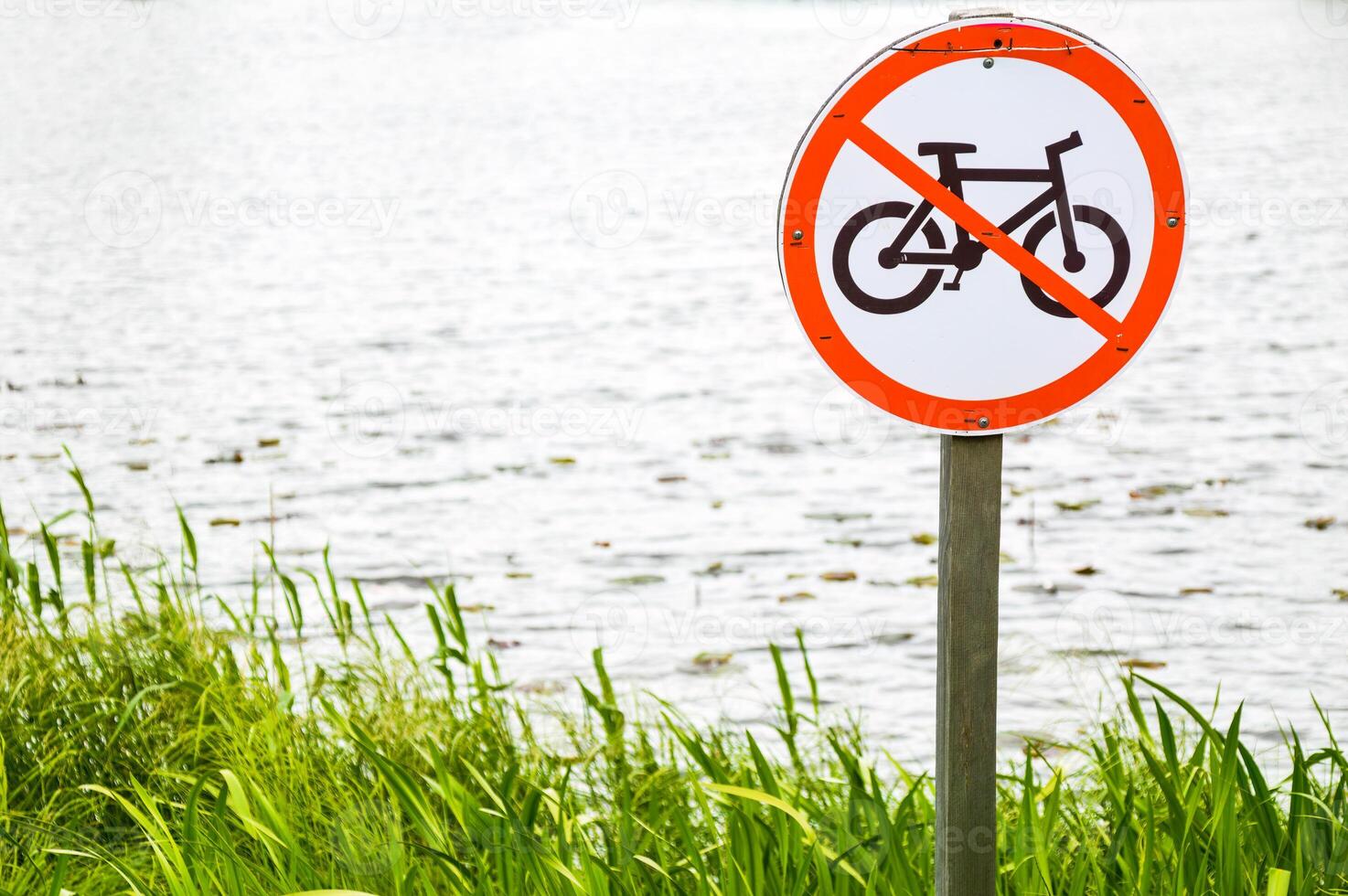 Bicycle prohibition sign on a green grass and water background in park photo