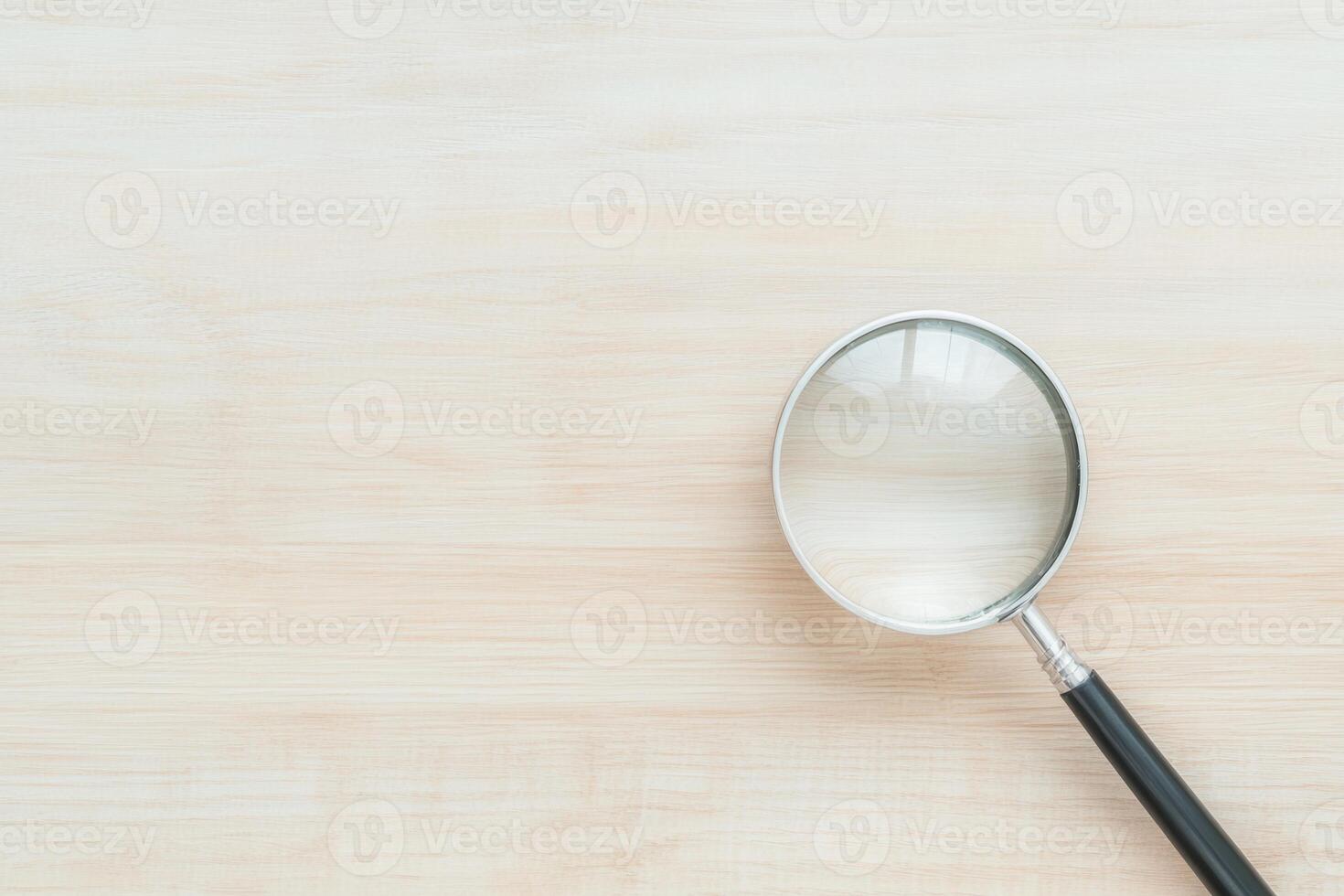 Close-up shot of a magnifying glass resting on a light, textured wooden surface, top-down view photo