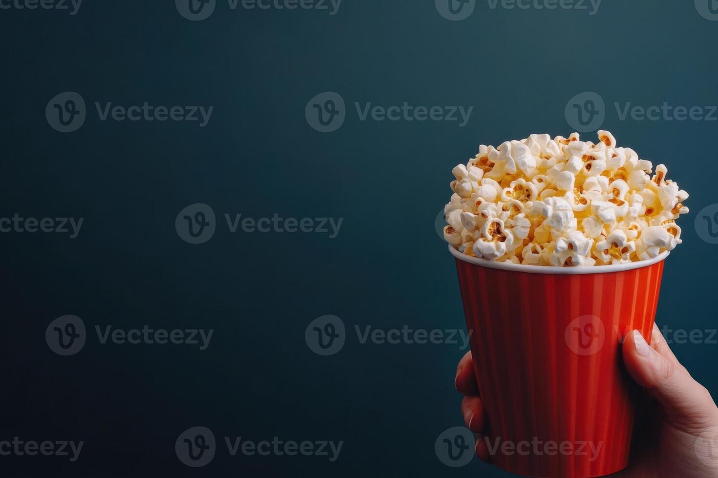 A hand holds a red and white striped bucket overflowing with fluffy, buttered popcorn snack photo