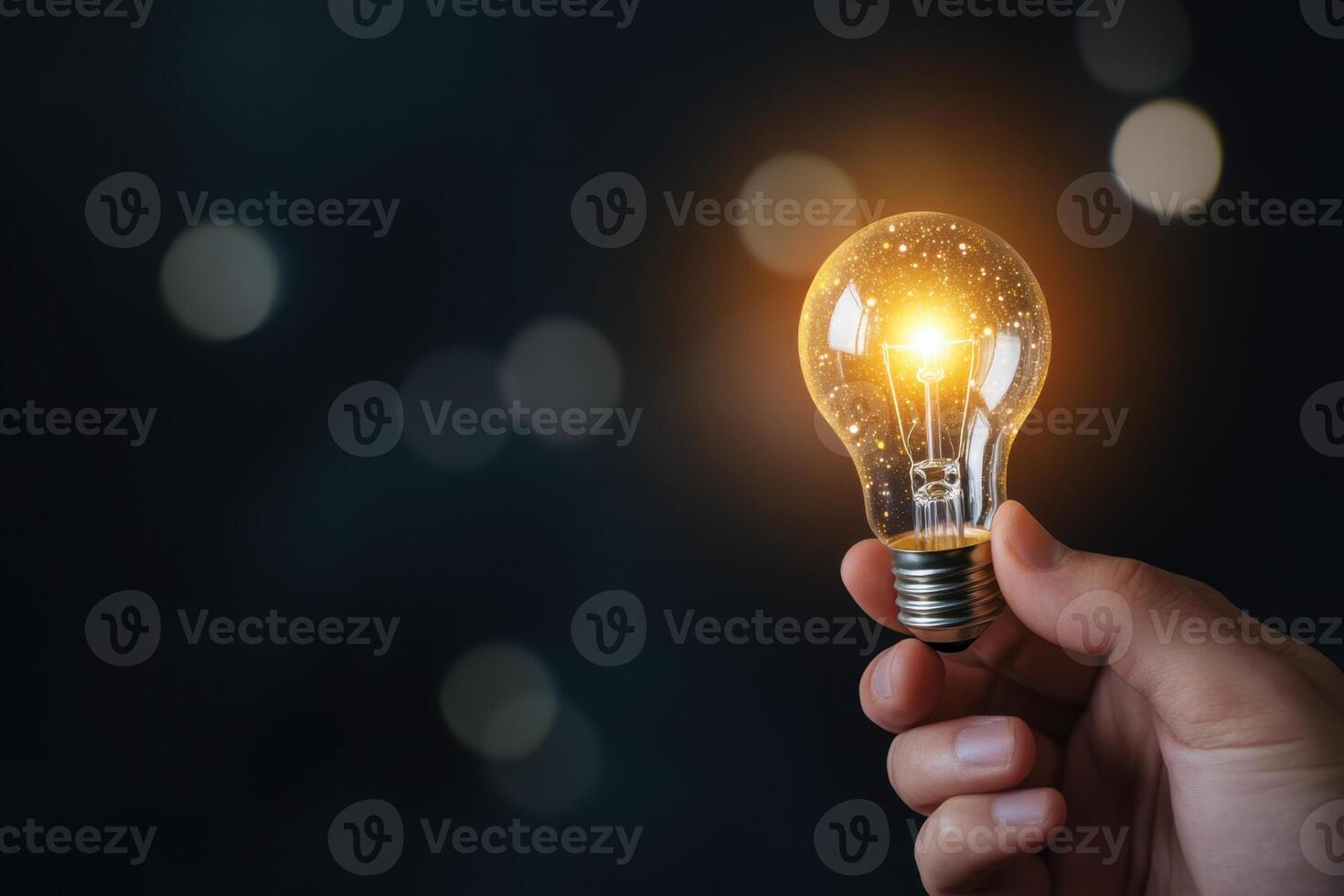 Illuminated lightbulb being held in hand against a dark background with blurred light effects photo