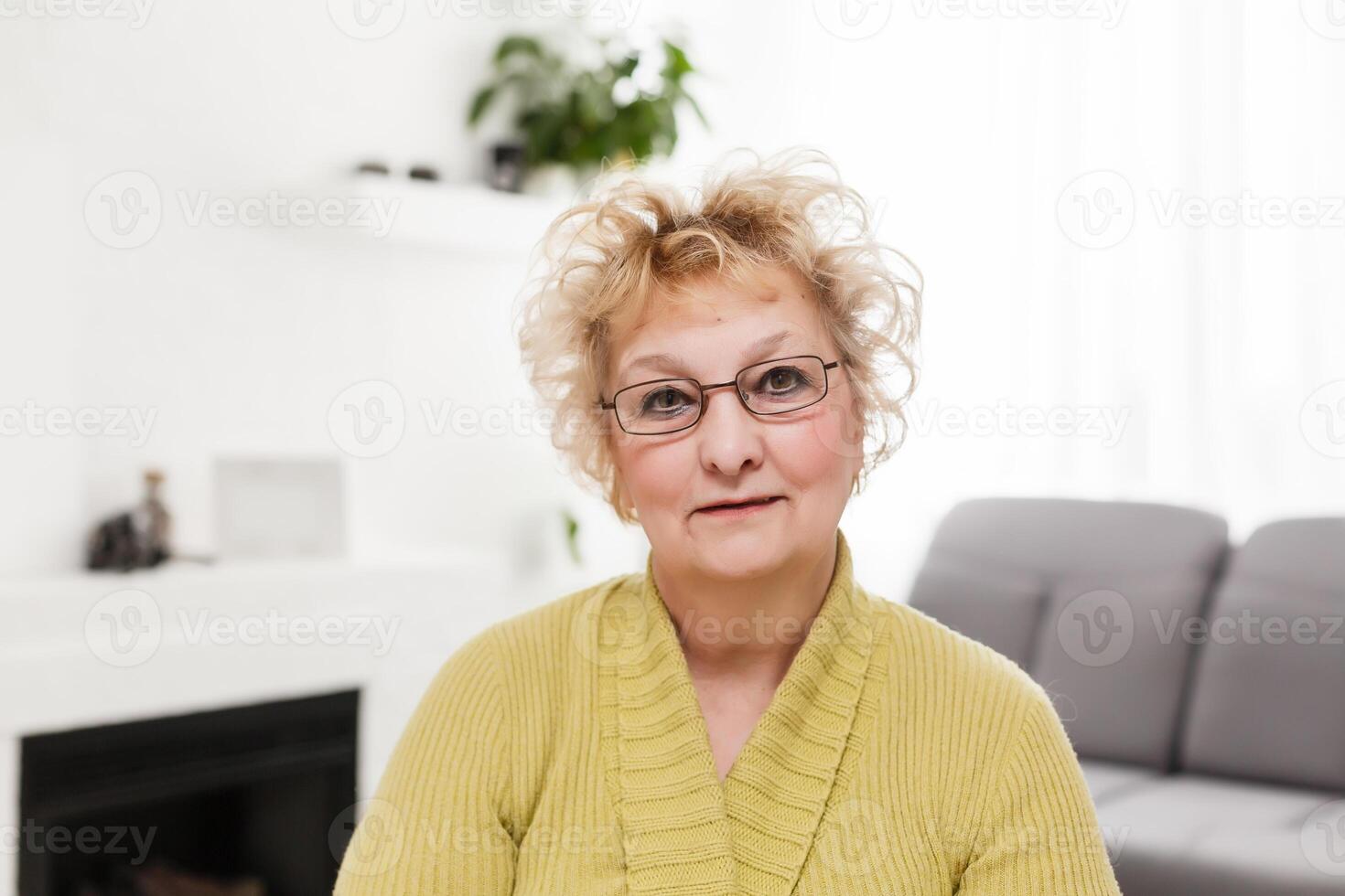 Attractive elderly woman sitting on couch at home, looking at camera, makes video call, communication distantly, modern wireless technologies concept photo