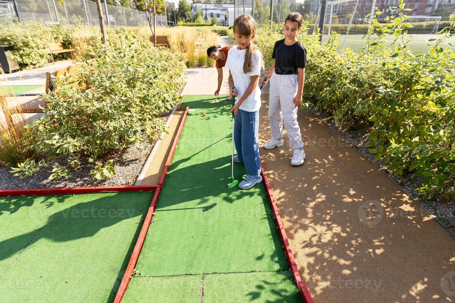 Cute school girl playing mini golf with family. Happy toddler child having fun with outdoor activity. Summer sport for children and adults, outdoors. Family vacations or resort. photo