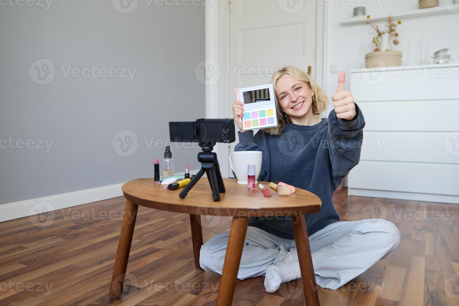 Portrait of beautiful smiling woman, recording in her room, has camera on coffee table, reviewing makeup, doing lifestyle vlog for social media account, records a tutorial photo