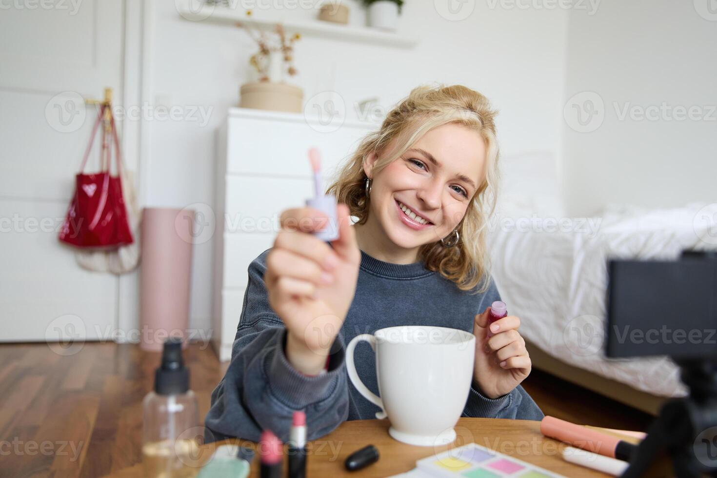 Portrait of smiling woman shows lip gloss, advertising makeup on her social media account, recording on digital camera, content maker working on new project in her room photo