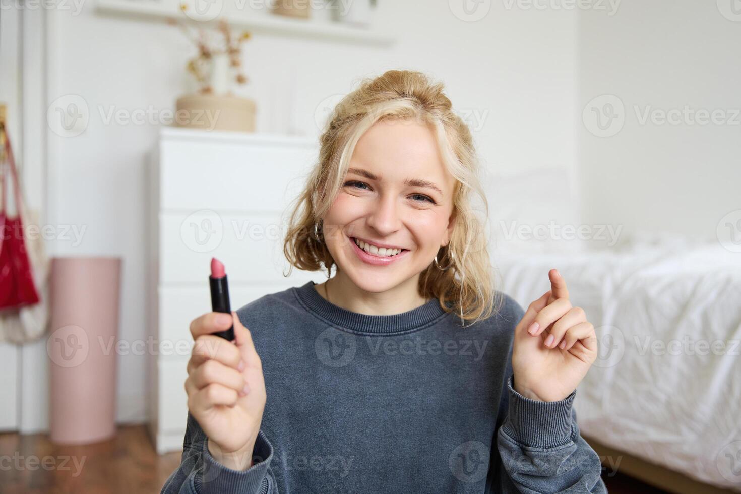 Portrait of cute, charismatic beauty blogger, woman sits in a room with lipstick in hand, talking about makeup, chatting with followers, recording online stream on social media app photo