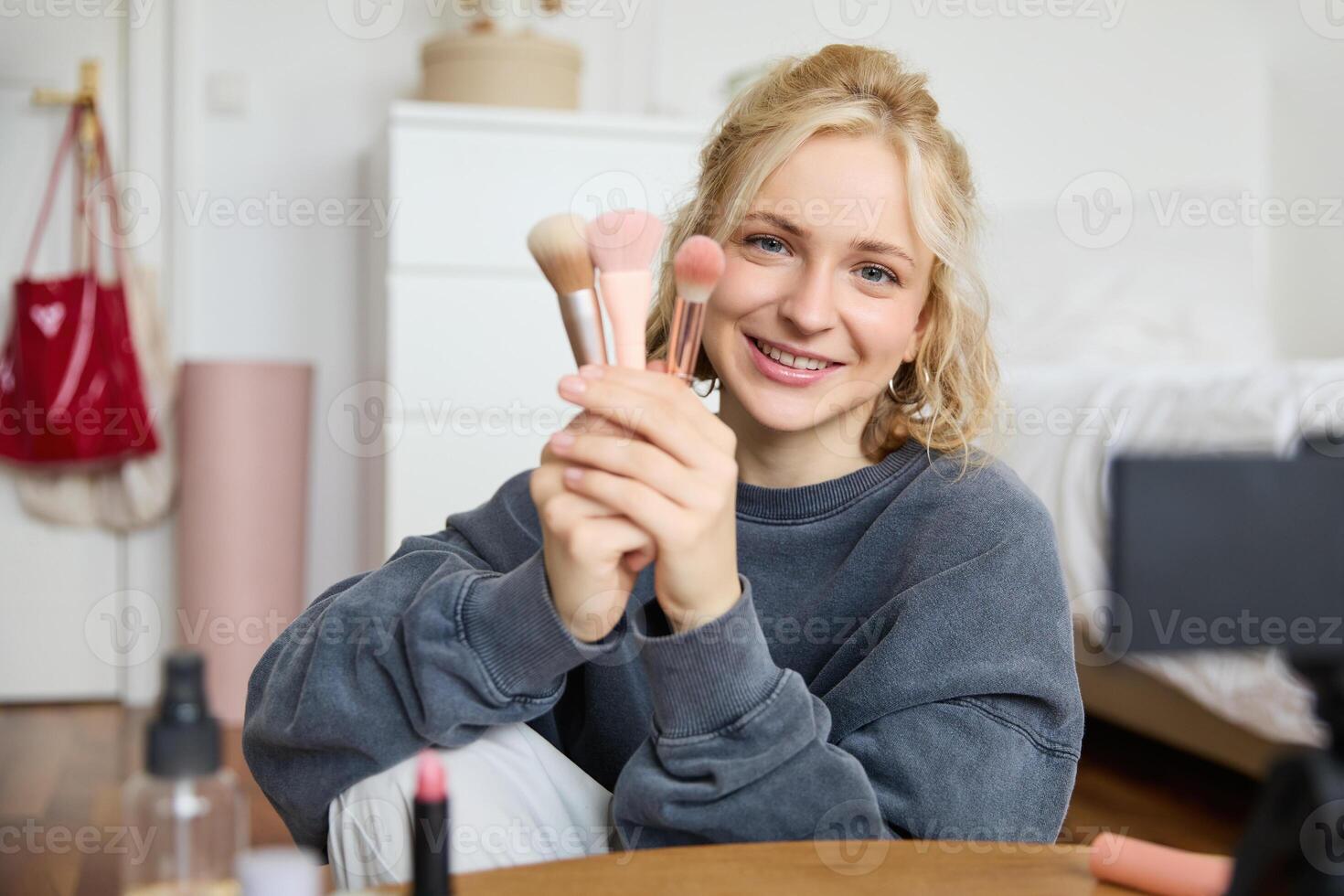 Portrait of content media creator, blogger sits in her room and records of her favourite makeup brushes, talks on camera photo