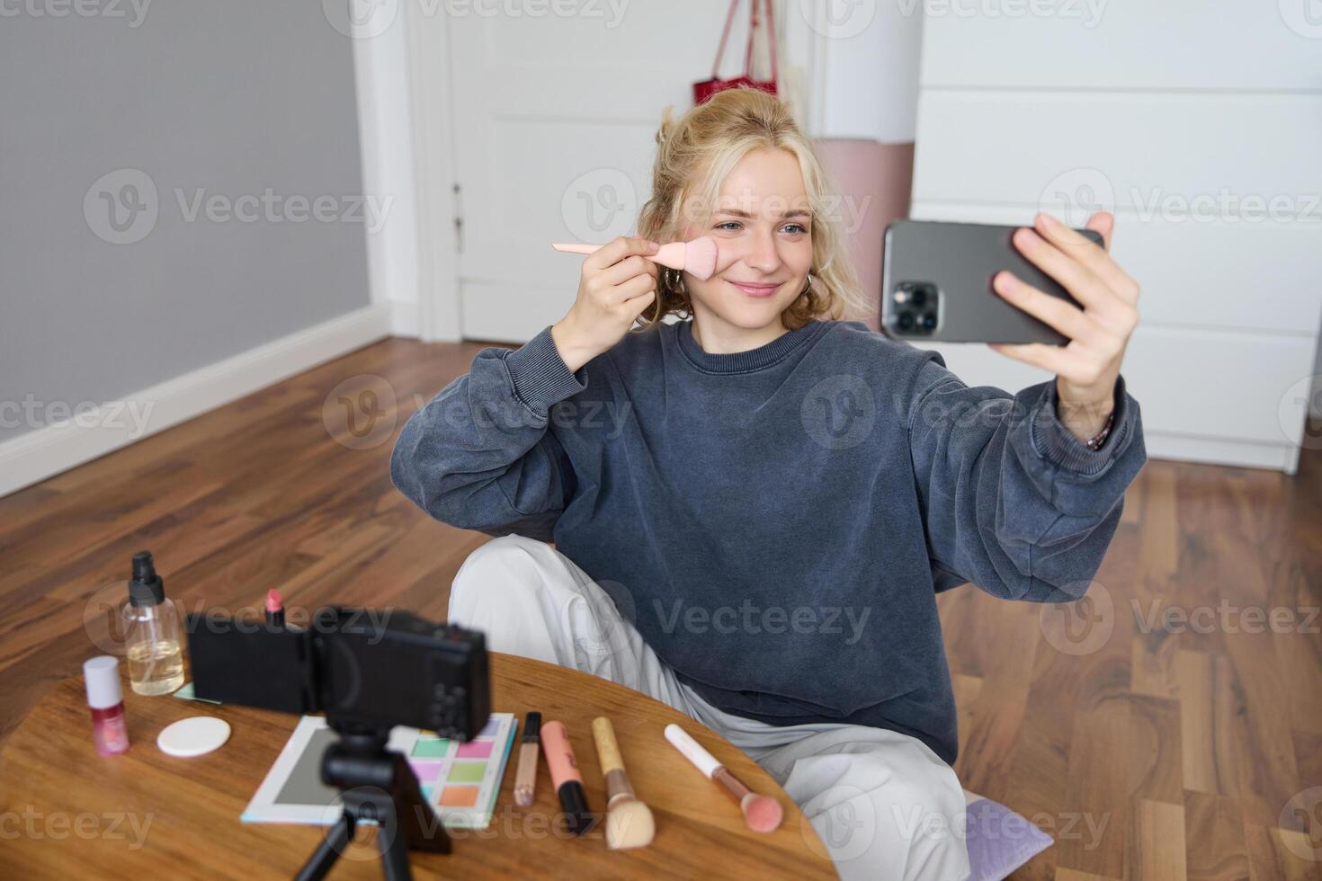 Portrait of beautiful blond girl doing makeup on camera, recording vlog using digital camera and live stream on mobile phone app, chatting with audience photo