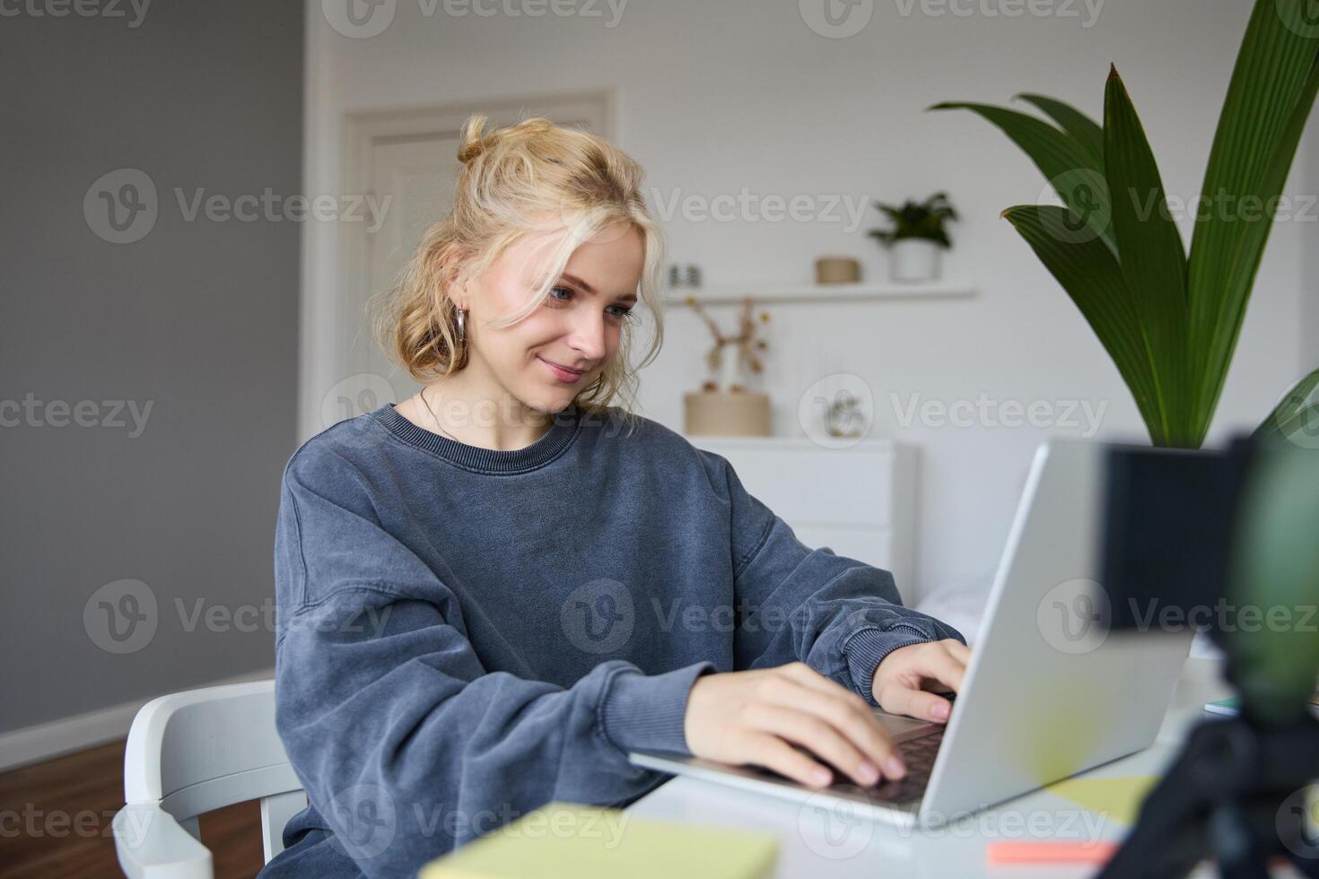 Portrait of young blond woman, female college student works from home on assignment, uses laptop, studies remotely, sits in room in front of computer photo