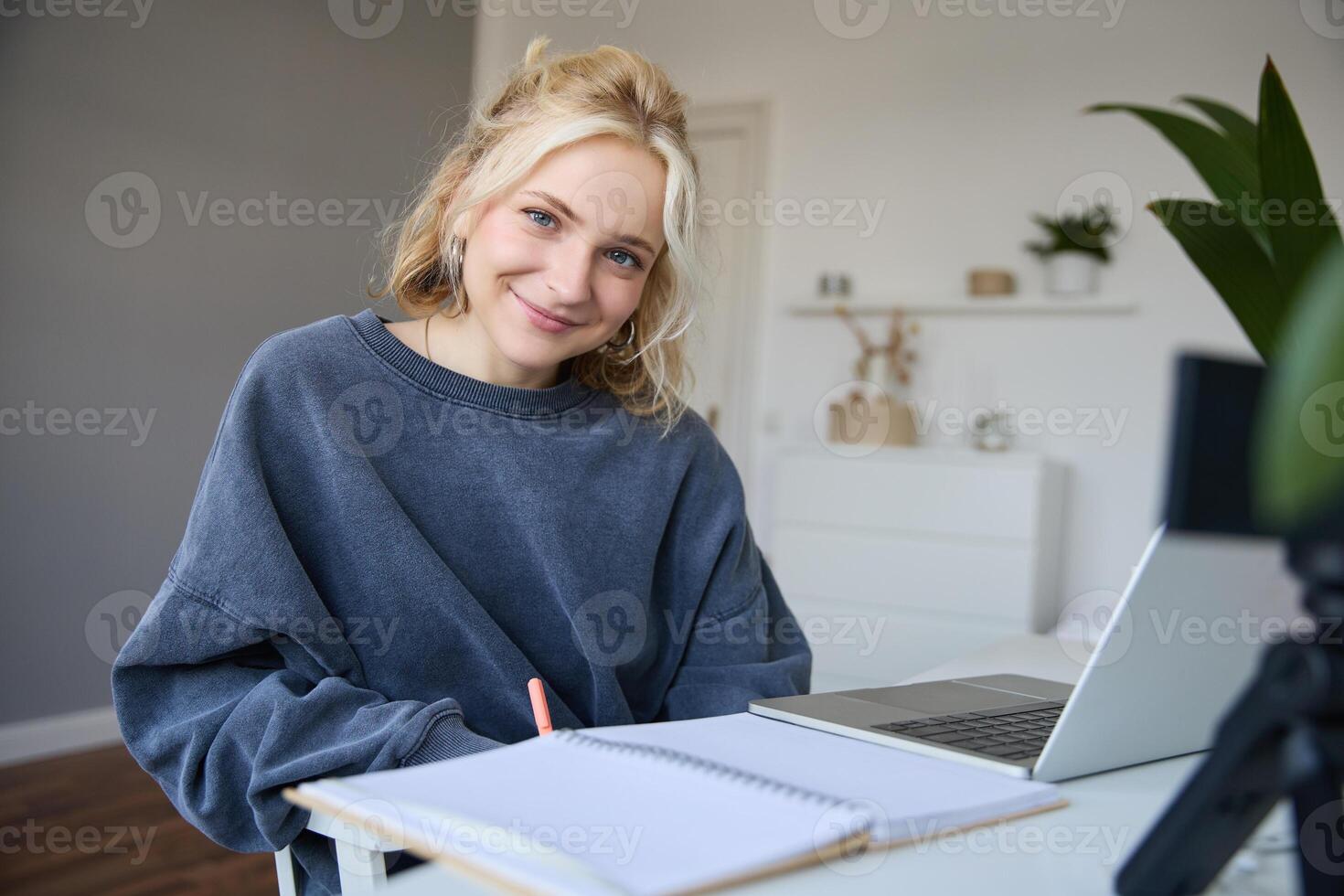 Portrait of beautiful smiling woman, student studying at home, remote education concept, sits in a room with laptop and writes down notes, uses her journal photo