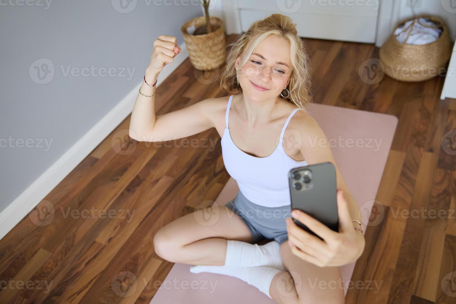 Portrait of young sporty woman taking selfie during workout training, content creator takes photos, shows muscles on camera, flexing biceps photo