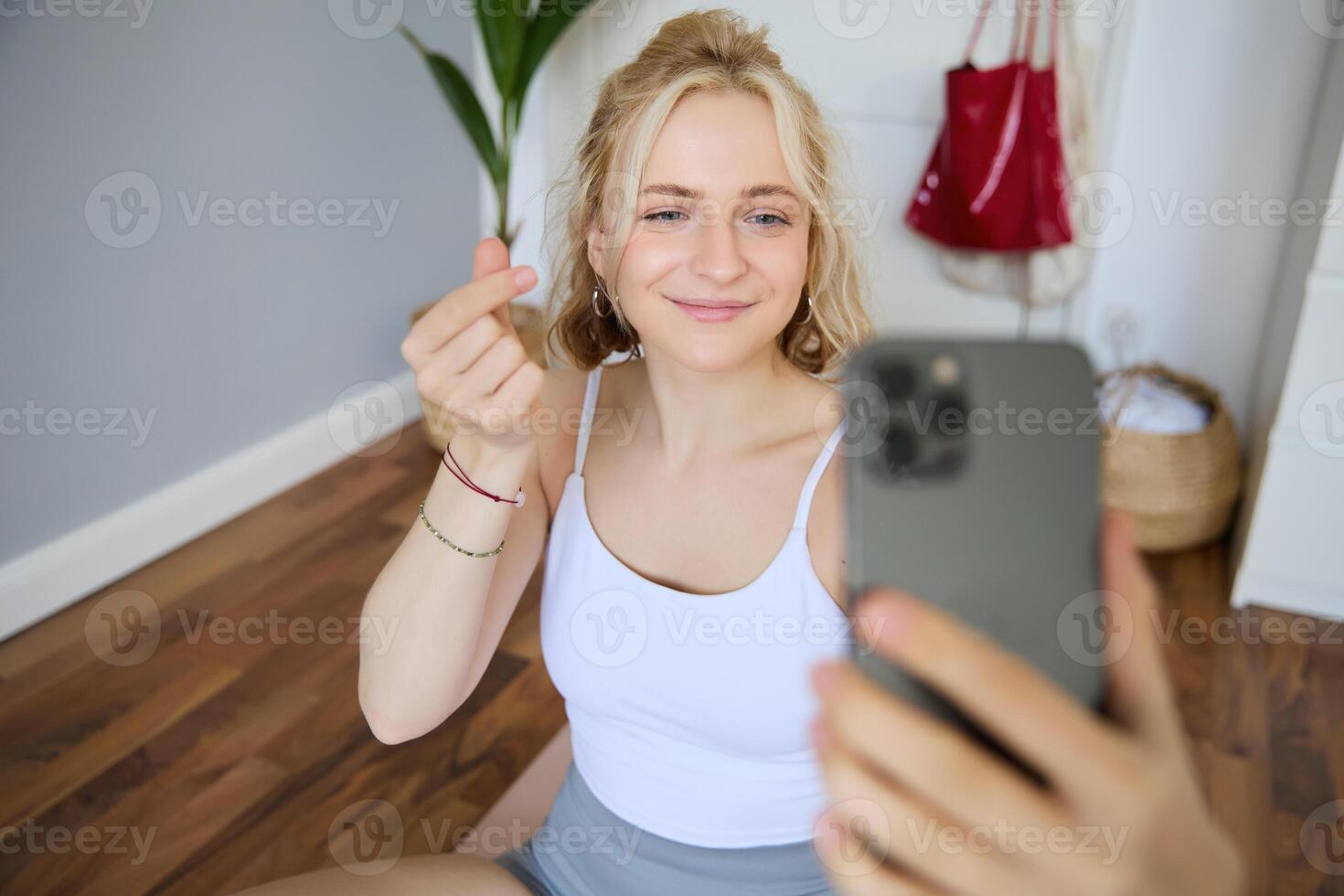 Portrait of young beautiful blond woman, fitness instructor doing exercises at home on yoga mat, taking selfies on smartphone, recording of herself for social media account about workout photo
