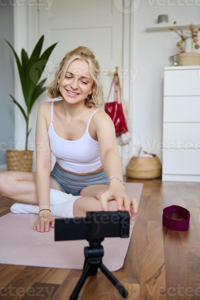 Vertical shot of athletic, fitness woman recording of herself on digital camera, creating content for social media about workout and home exercises photo
