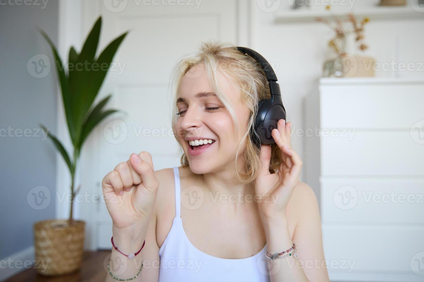 Portrait of happy woman, listens to music in wireless headphones, holding invisible microphone, singing into mic, smiling, enjoying good sound quality photo