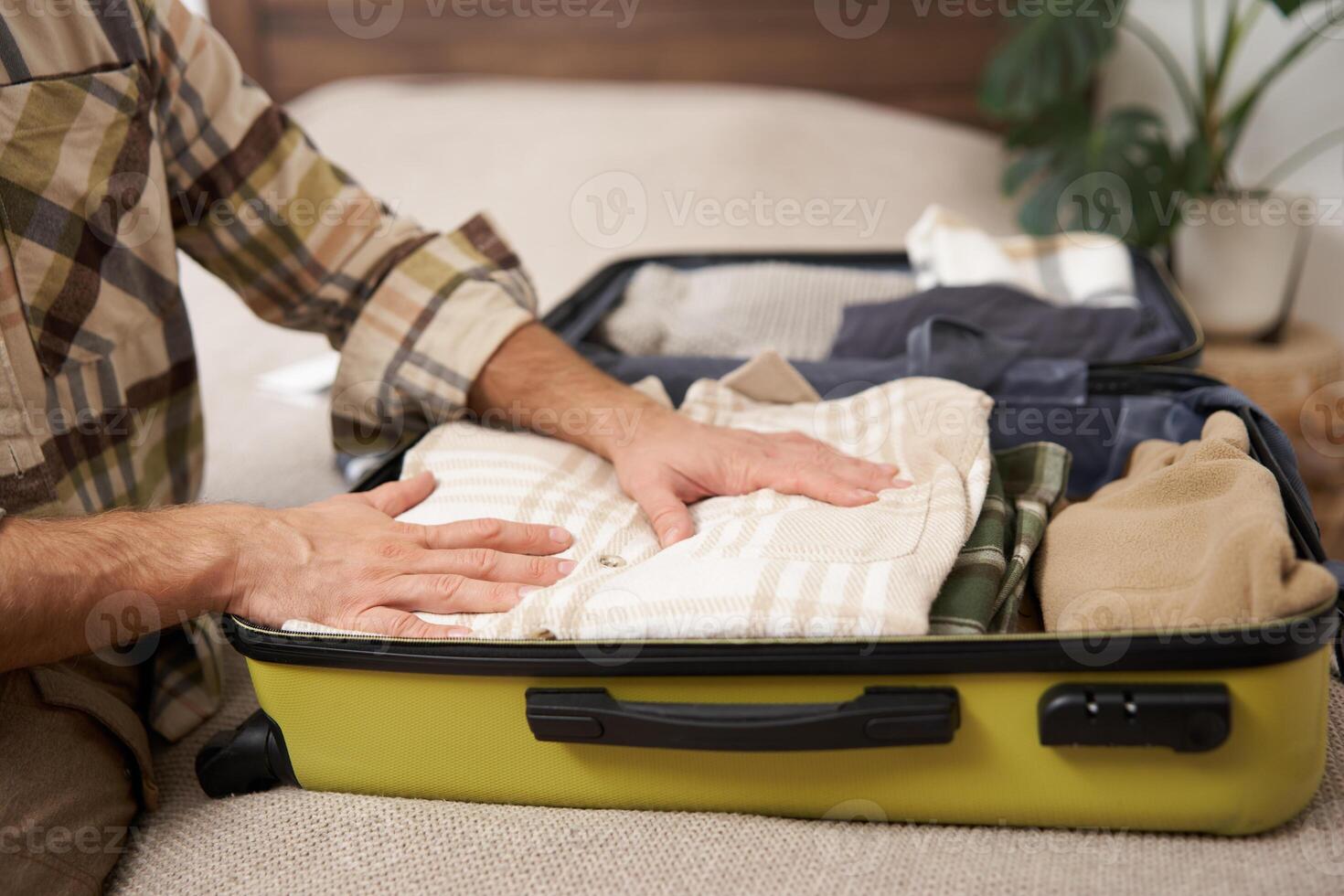 Male hands, tourist packing his clothes in luggage, putting items inside suitcase, getting ready for a vacation, going on holiday or business trip photo