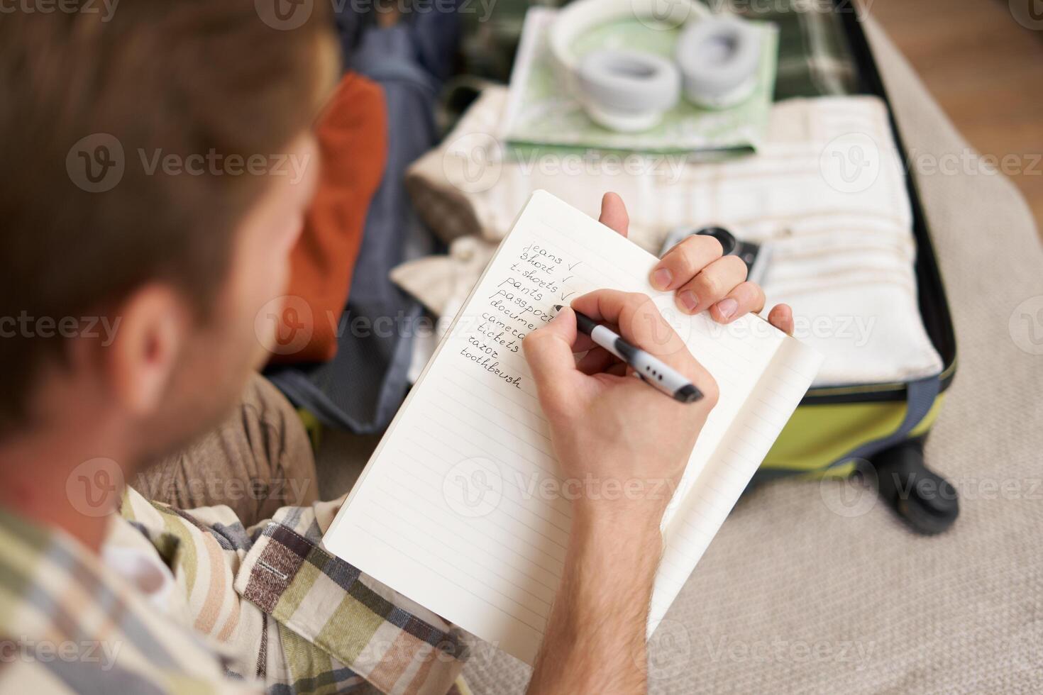 Close up portrait of man packing suitcase, making notes, check-list of items he wants to take on holiday, packing luggage photo